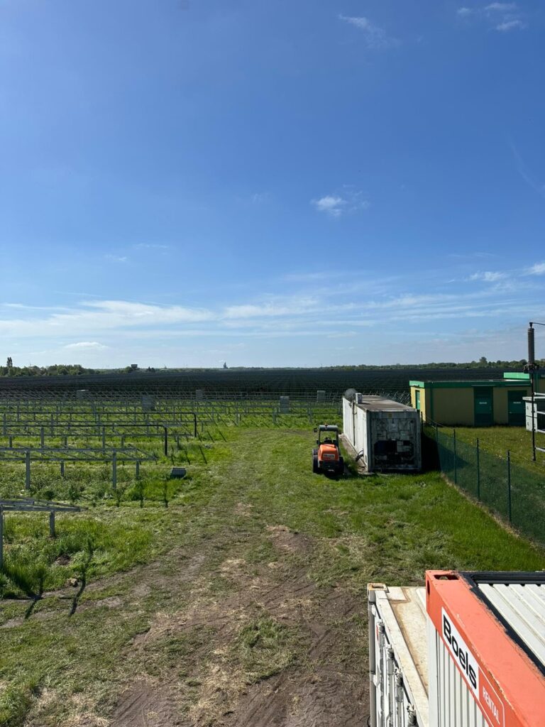 Blick auf eine gepflegte Wiese mit Traktor, Nebengebäuden und solarbetriebene Anlagen unter klarem Himmel.