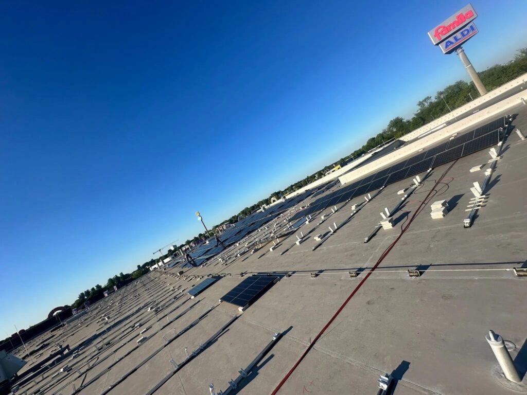 Dachansicht mit Solarzelleninstallation auf einem Einzelhandelsgebäude, im Hintergrund ein Aldi-Schild und blauer Himmel.